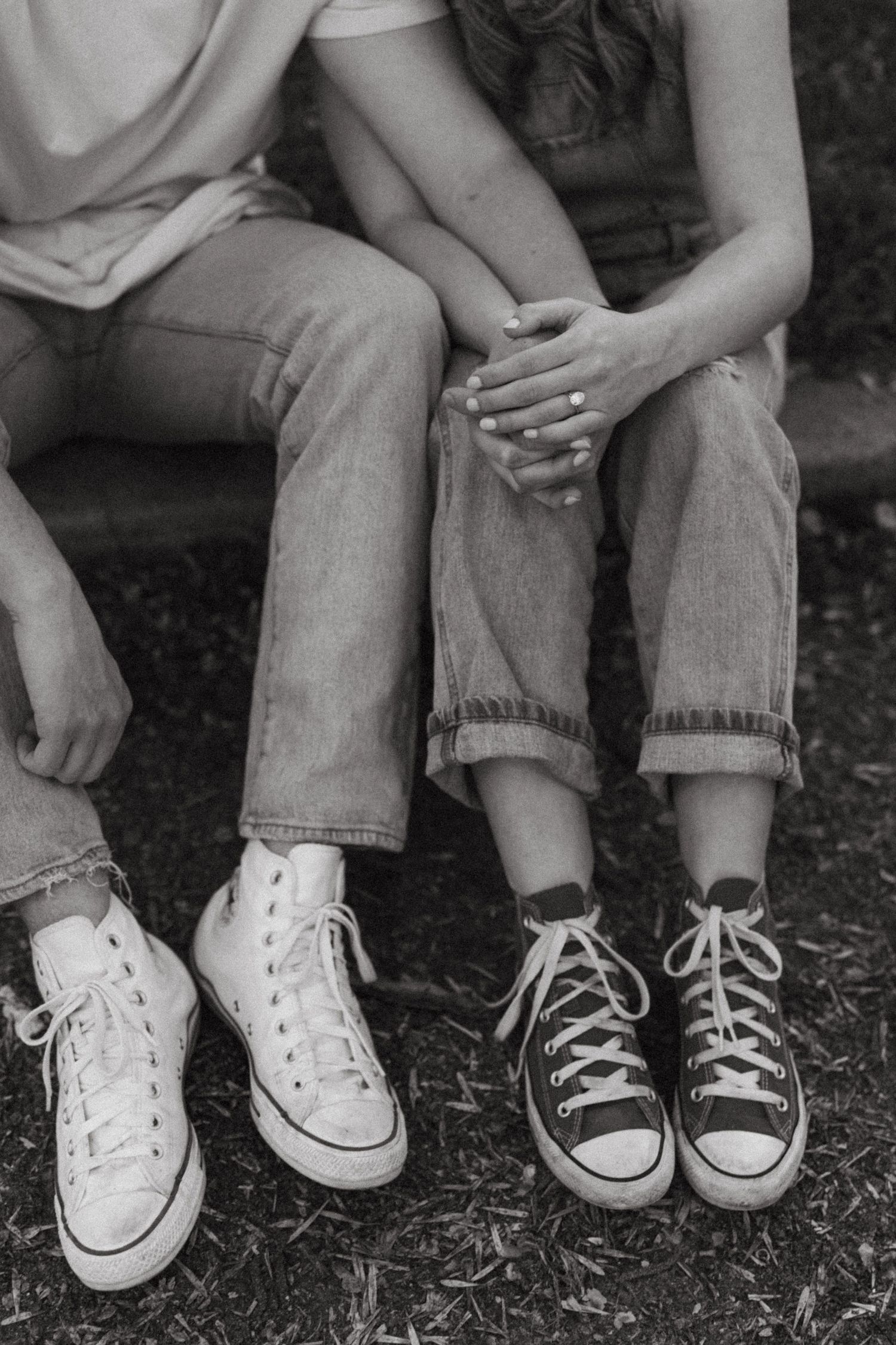 Black and white photo of two pairs of Converse sneakers, one white and one black, worn with rolled jeans.