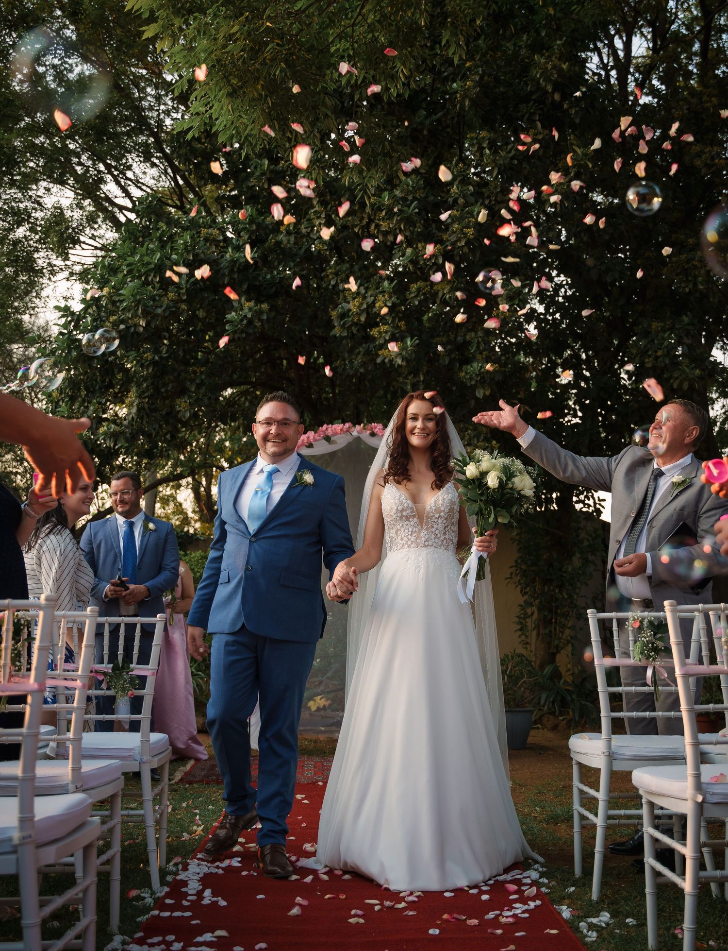 Wedding ceremony exit with rose petals being tossed as couple walks down aisle.