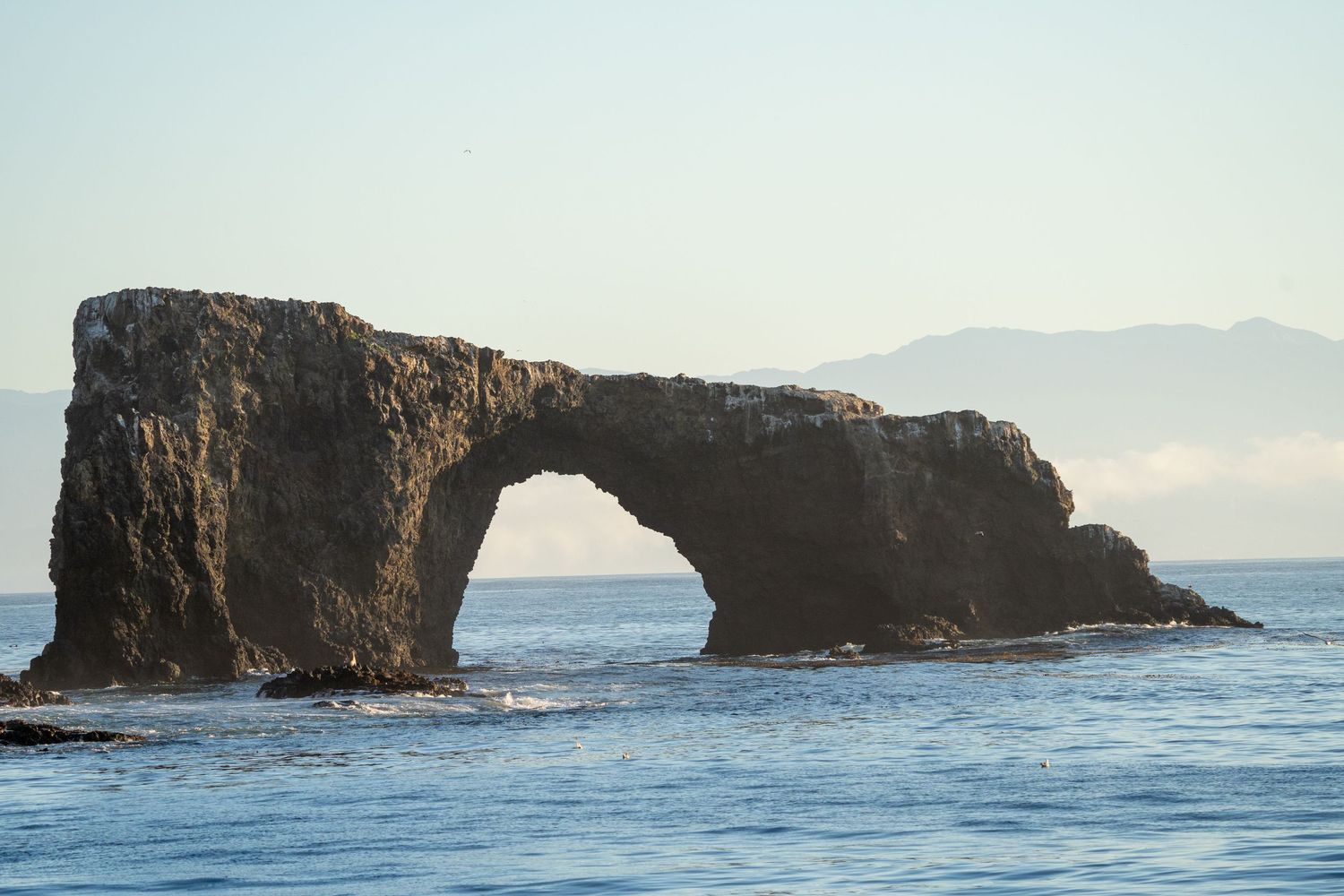 Natural rock arch formation at Anacapa Island, California, surrounded by clear blue ocean waters under a sunny sky