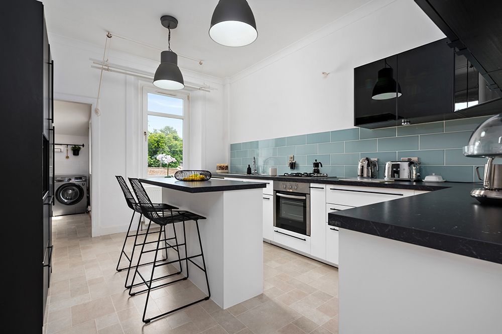 Modern white and black kitchen with blue backsplash features sleek countertops, pendant lights and bar seating.