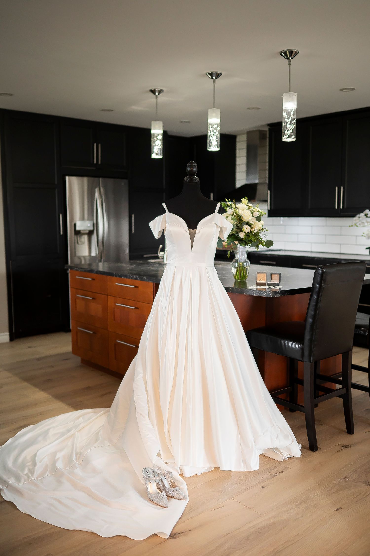 Elegant white wedding dress displayed in modern kitchen with pendant lighting.