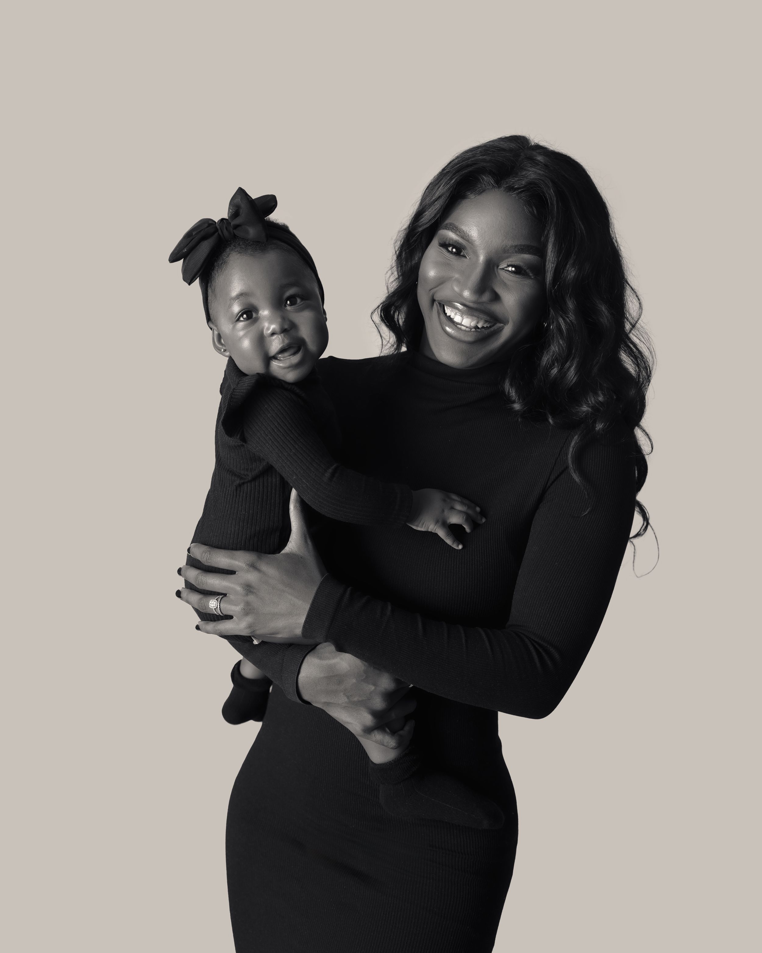 A heartwarming black and white portrait of a parent and baby in matching dark outfits.