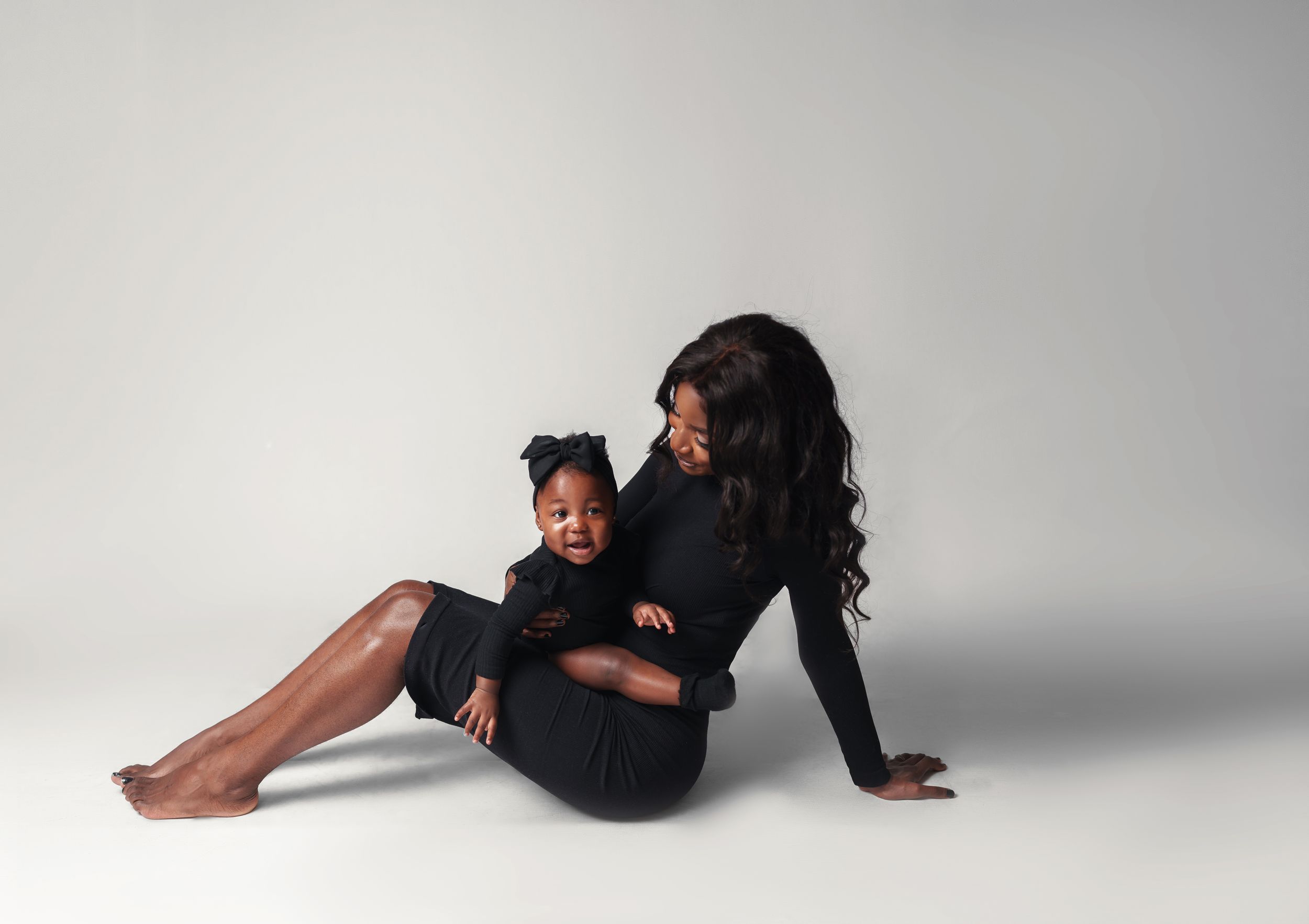 An intimate black and white portrait of a parent and child in dark clothing on the floor.