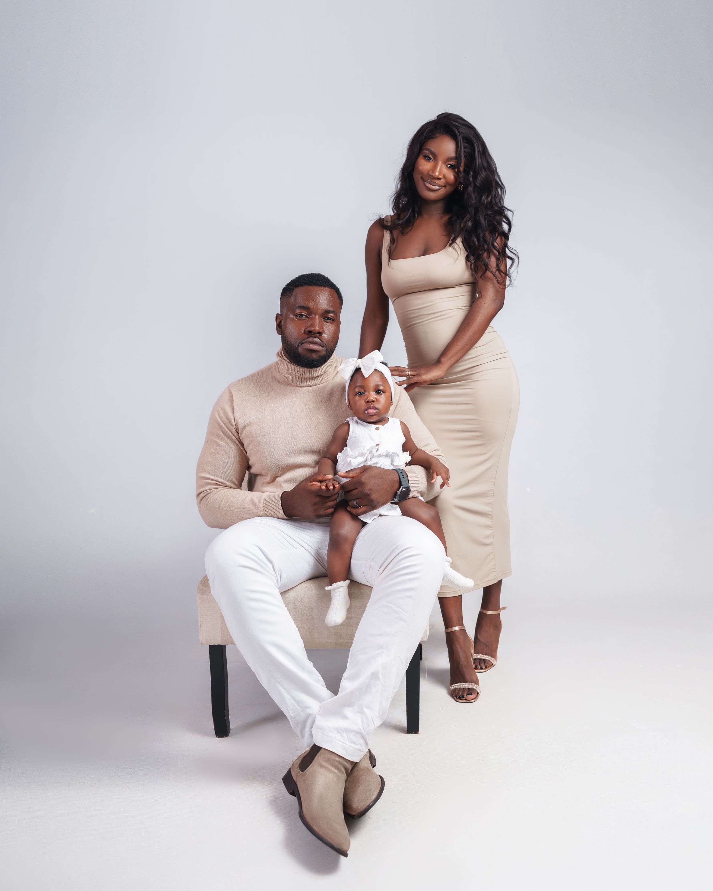 Studio portrait of family in matching beige and white outfits seated against grey backdrop.