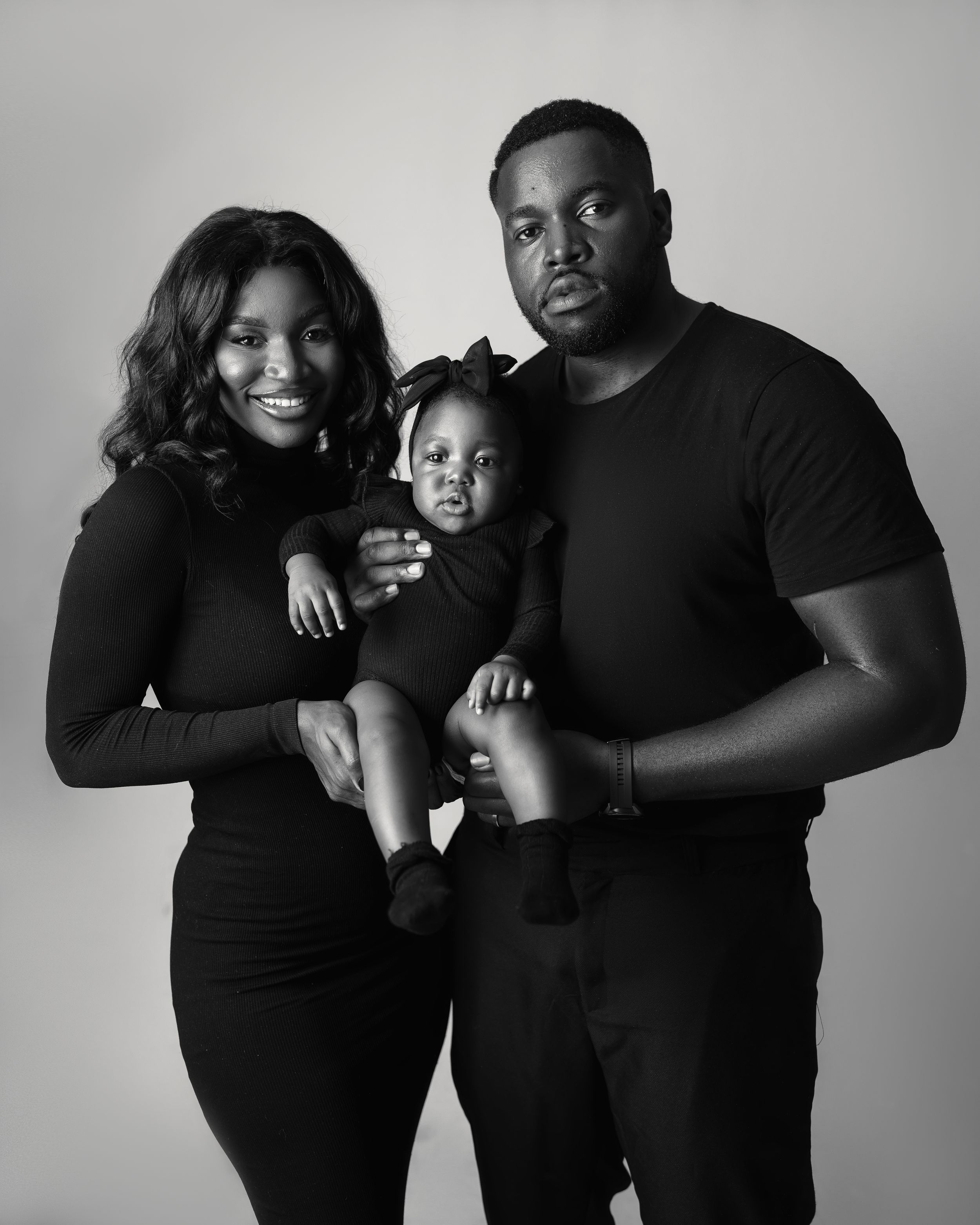 A black and white studio portrait of a family of three wearing coordinated dark outfits.