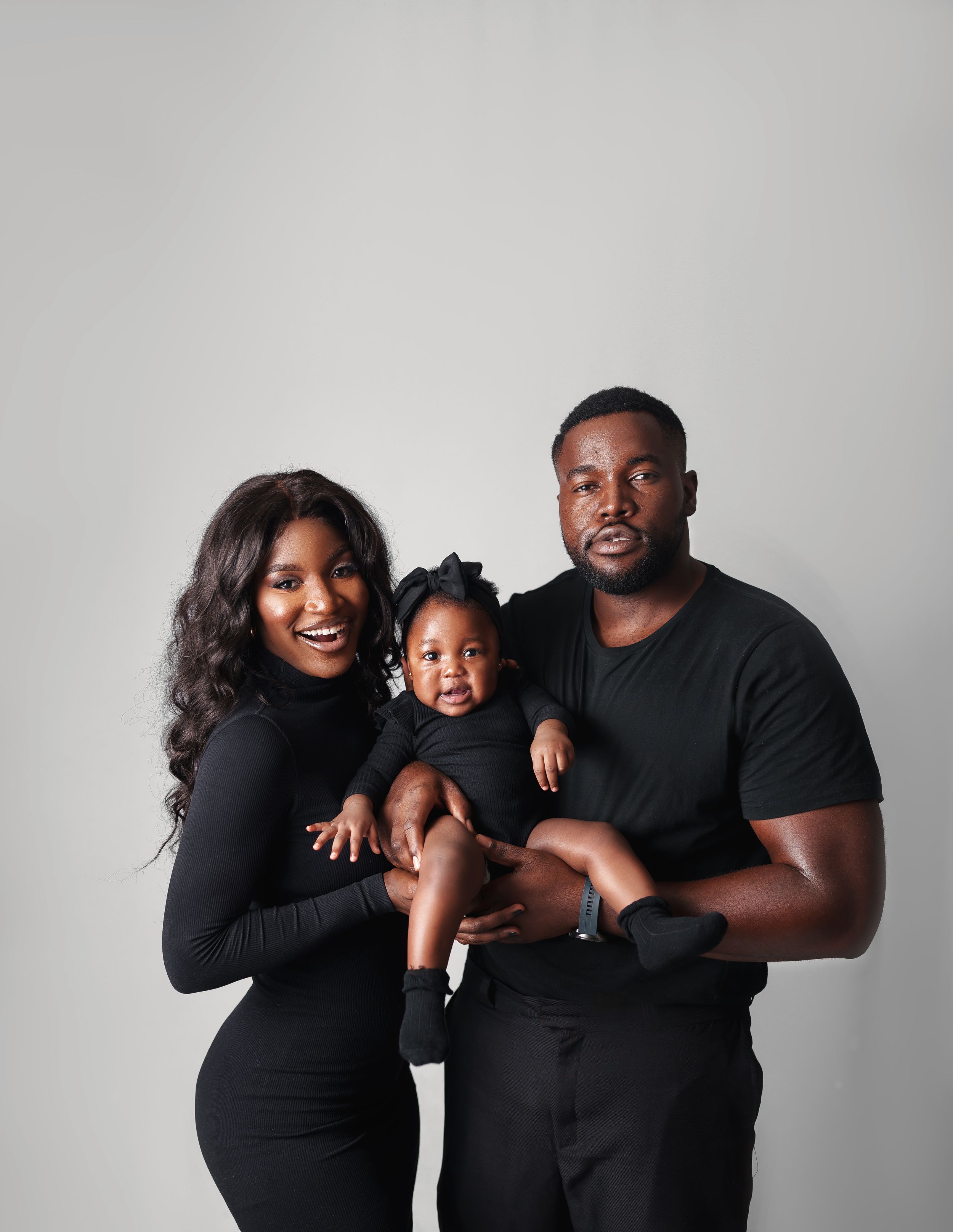 A modern family portrait with all members wearing black against a light gray background.