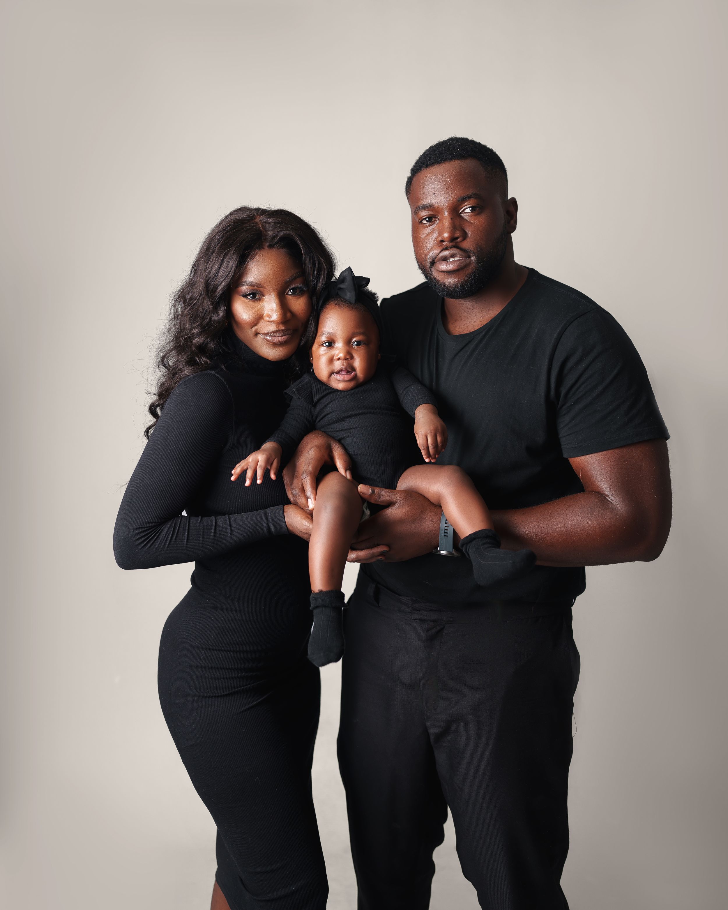 A studio portrait of a family in matching black outfits against a neutral background.