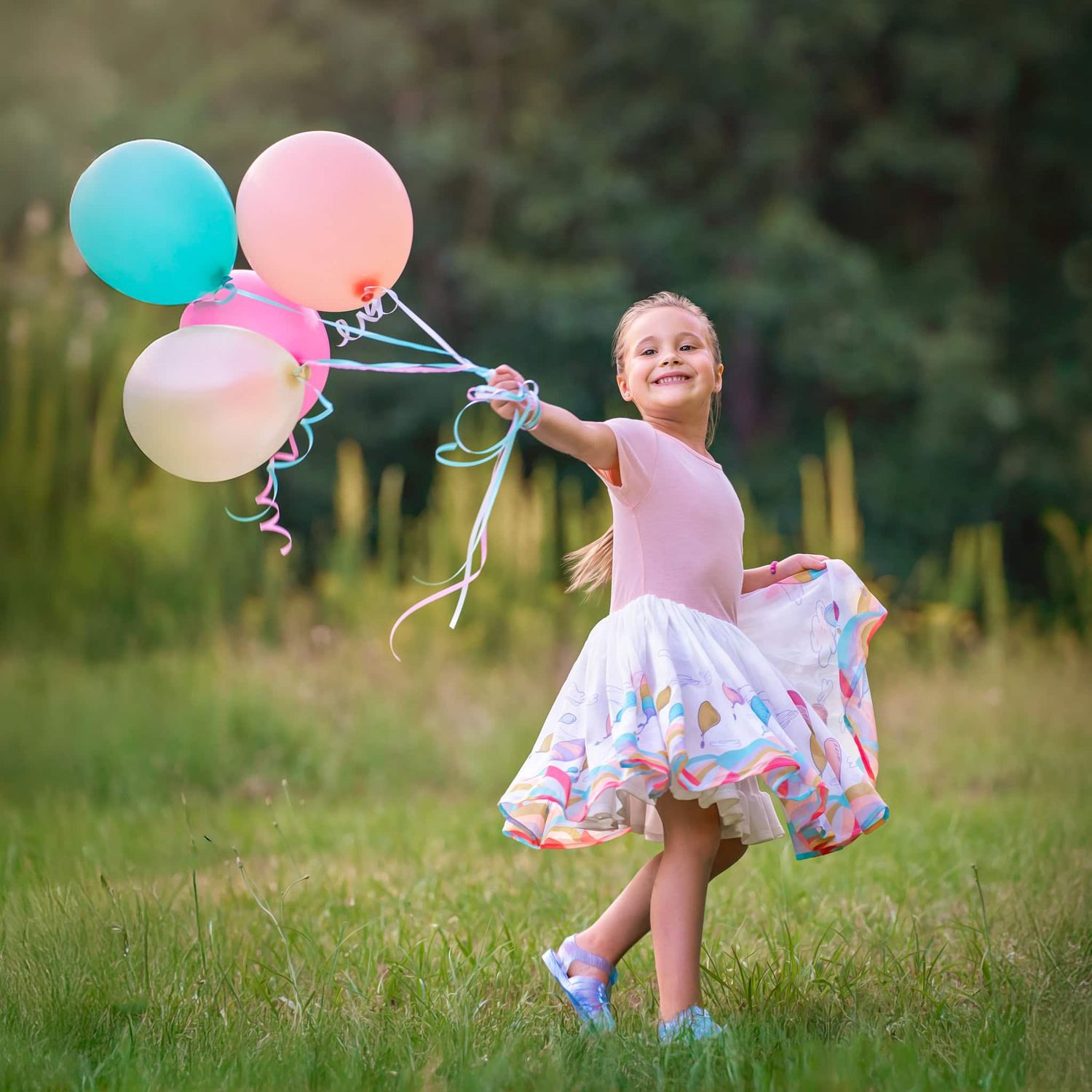Five-year-old girl in billowy Dr Seuss dress running through a yard holding pastel balloons flowing in the air