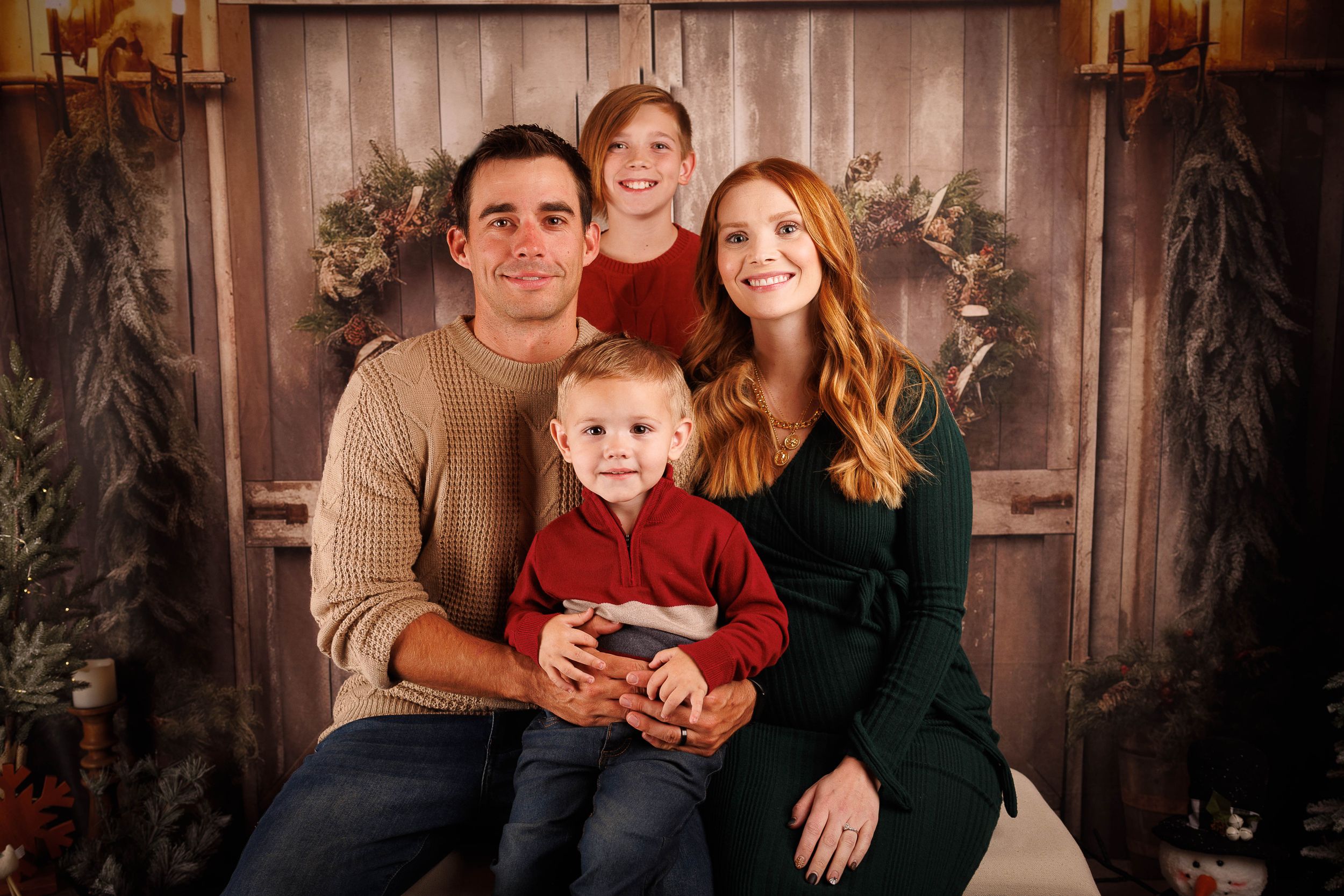 A family poses together for professional portraits against a rustic wooden backdrop in coordinating burgundy outfits.