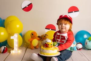 Colorful first birthday party setup with Pokemon theme featuring yellow and red decorations, cake, and balloons.