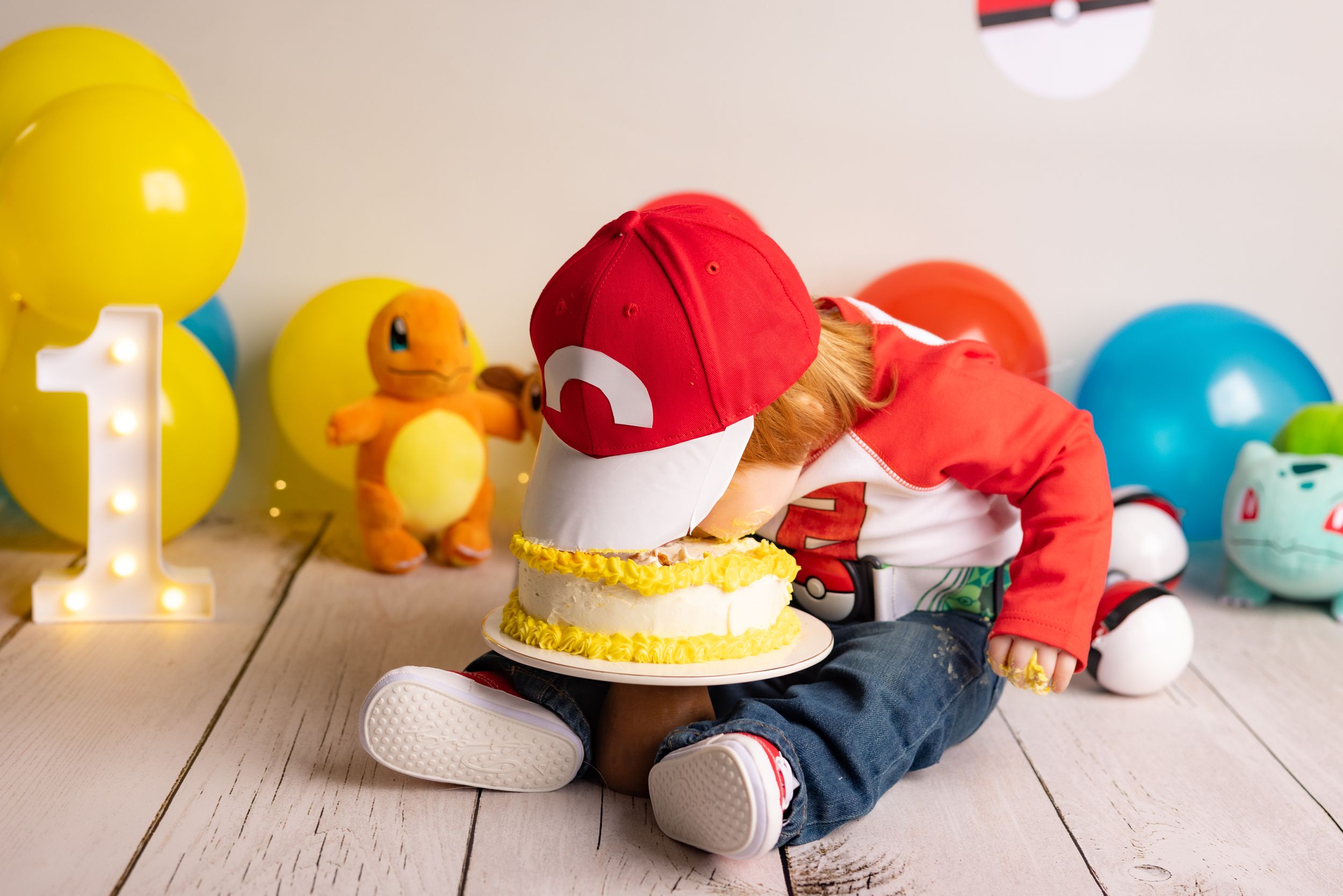 Colorful first birthday party setup with Pokemon theme featuring yellow and red decorations, cake, and balloons.