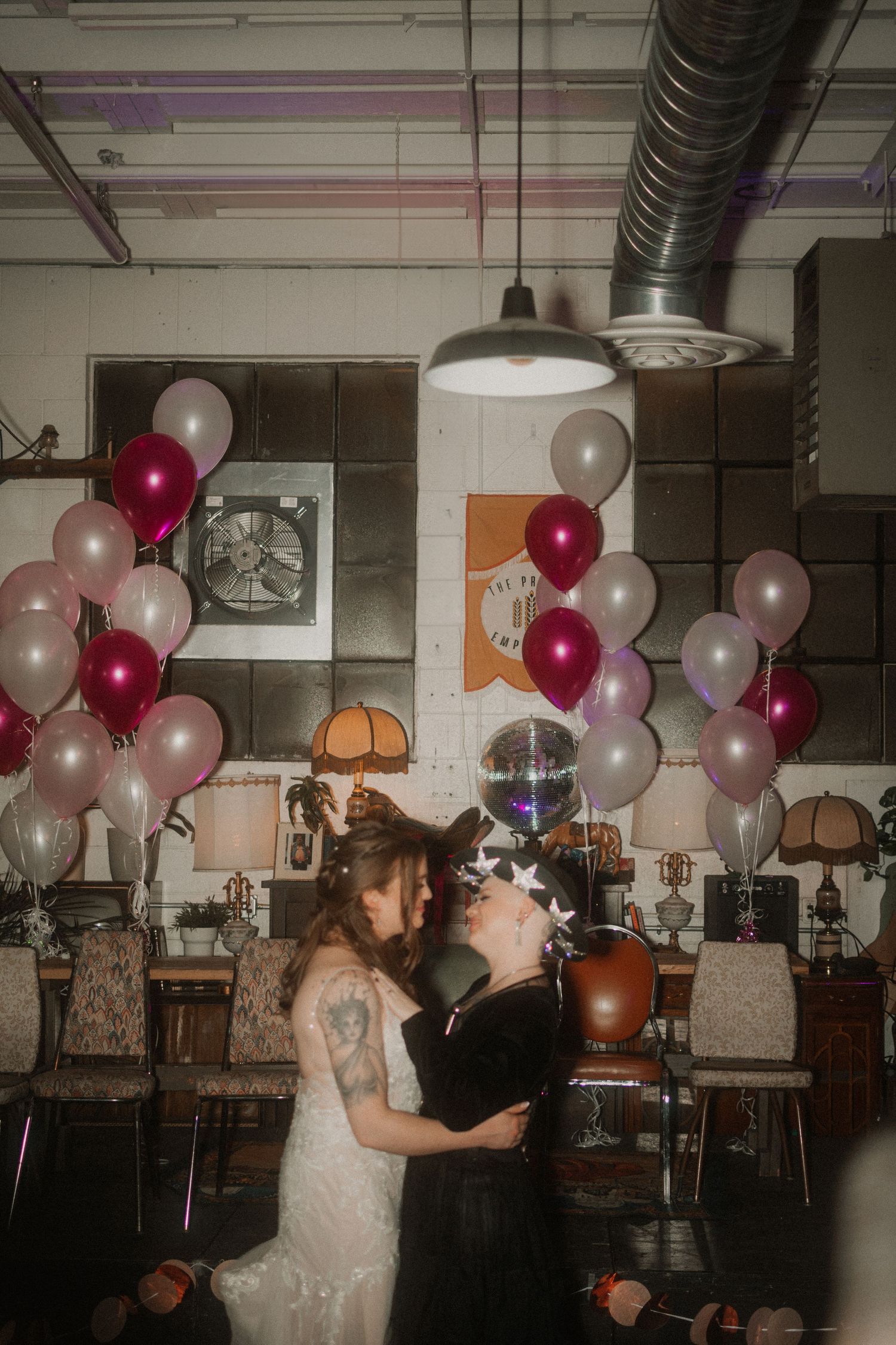 A romantic party scene with pink and white balloons decorating an industrial-style venue.