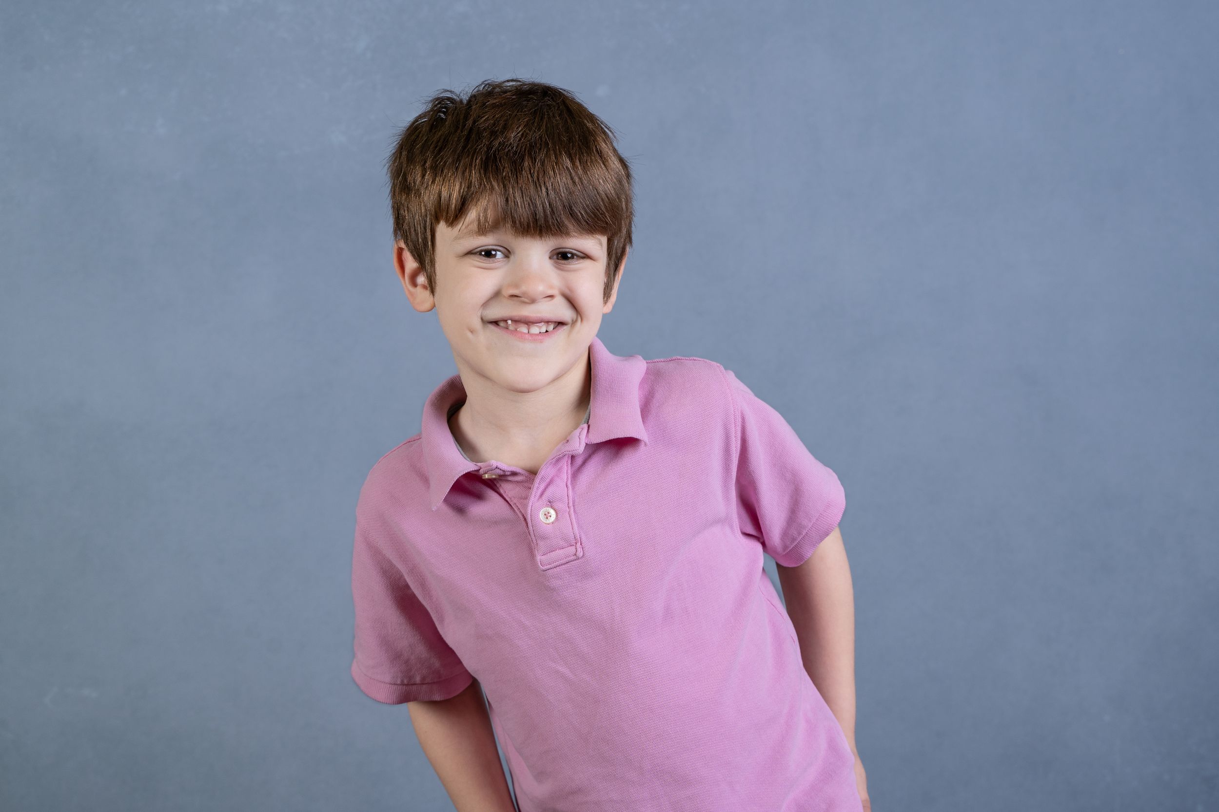 Studio portrait of young person in pink polo shirt against blue background.
