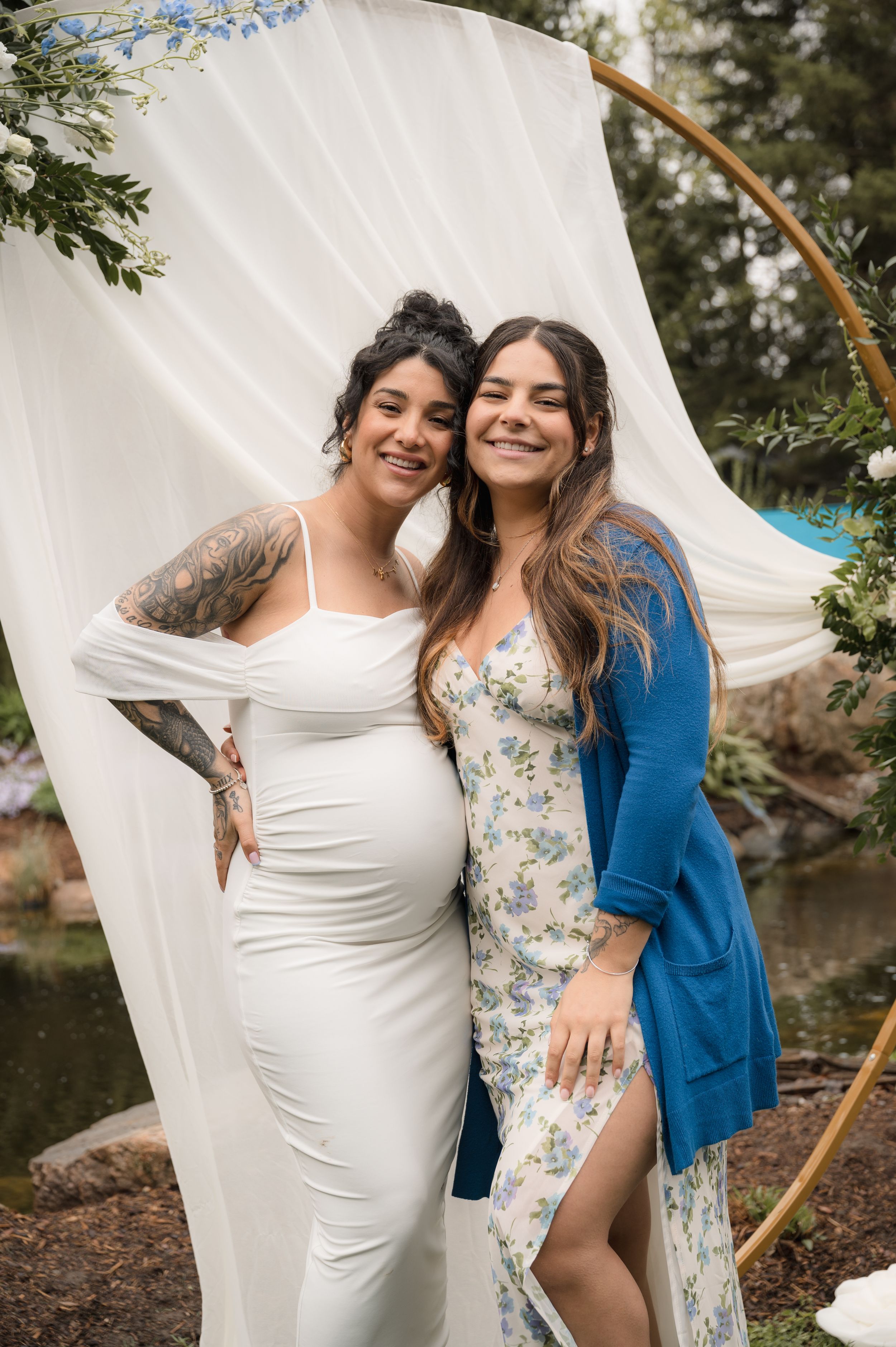 Two people posing together at an outdoor event with floral decorations and white draping.