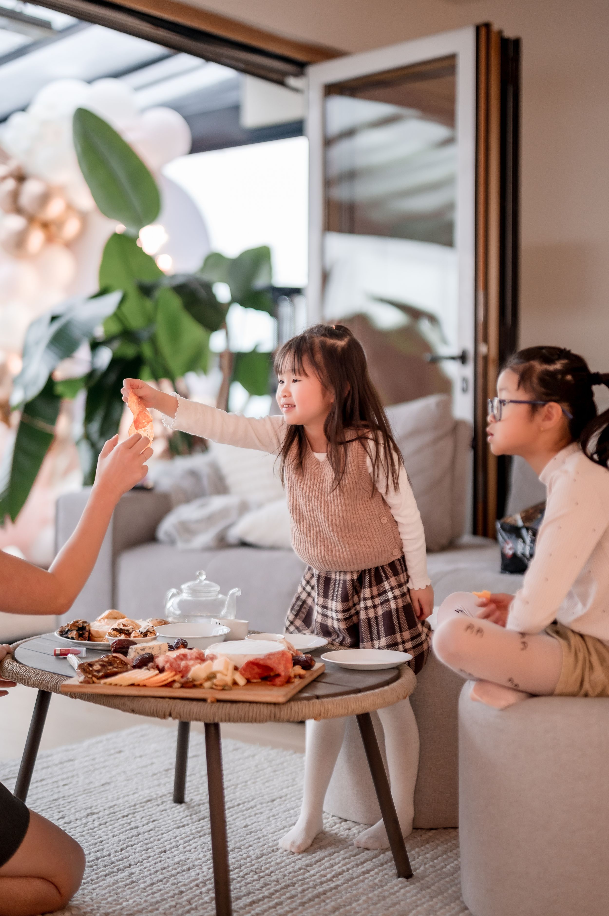 Friends enjoying tea and snacks at a low table with elegant party decorations and balloons in the background.
