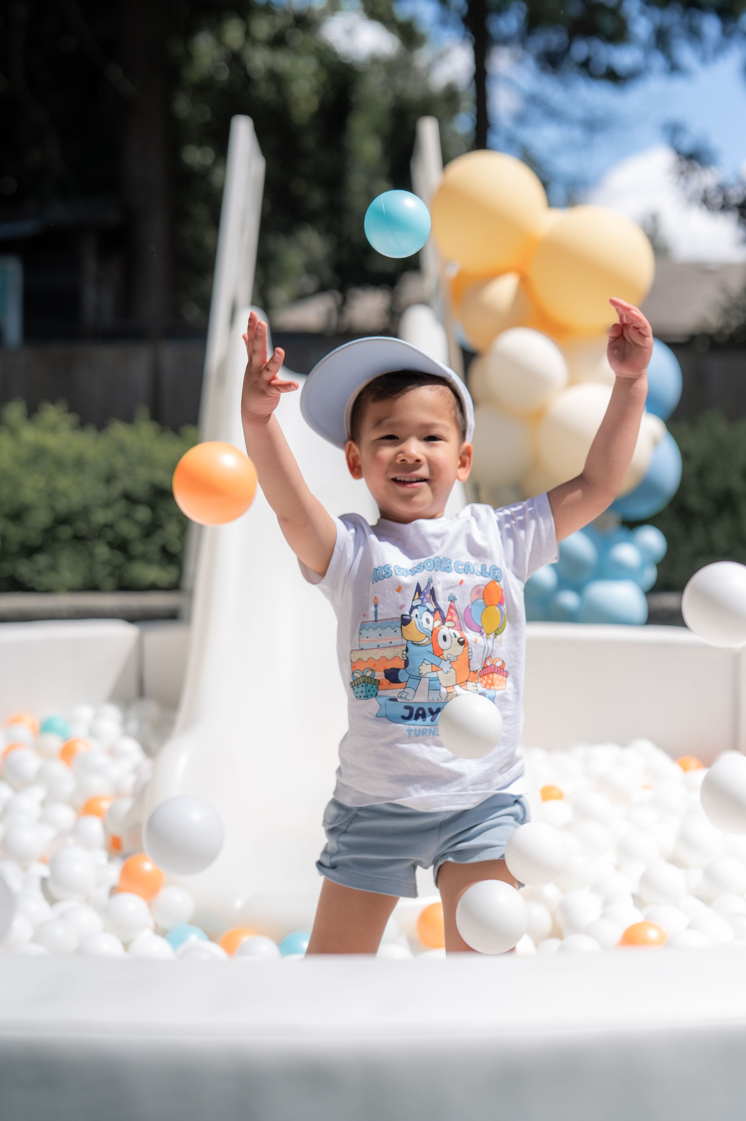 Happy toddler plays in bubbles and balloons outdoors with orange and blue party decorations during a summer celebration.