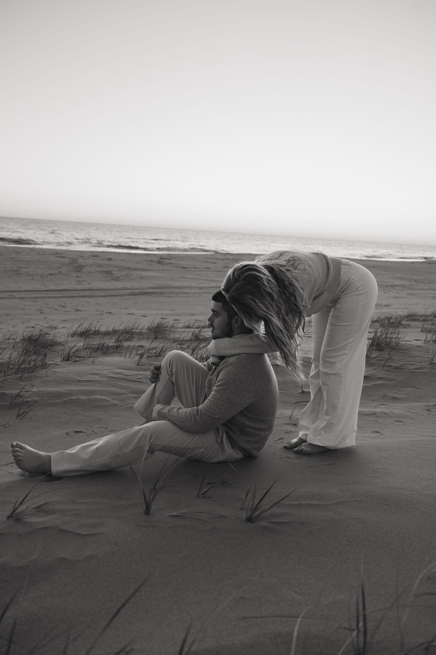 Black and white photo of two people sharing intimate moment on beach at sunset.