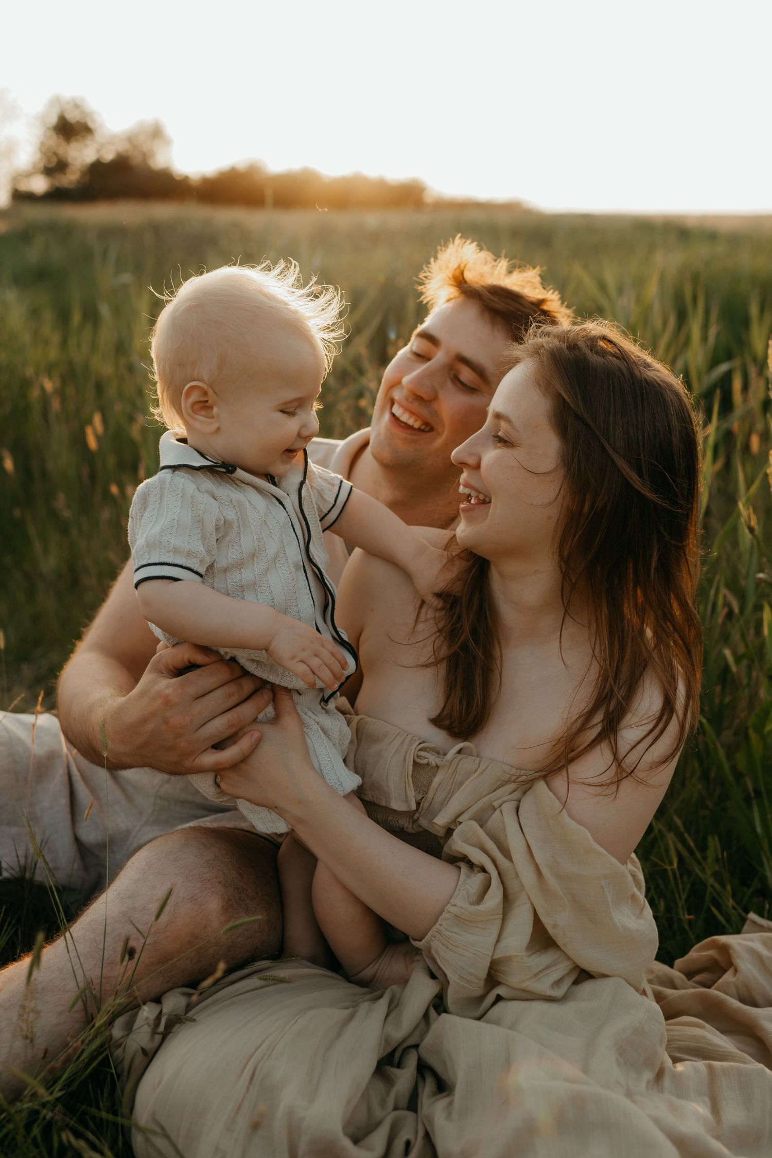 a family of three laughing in a field during a family session with Forever Ours Photography kent family photographer