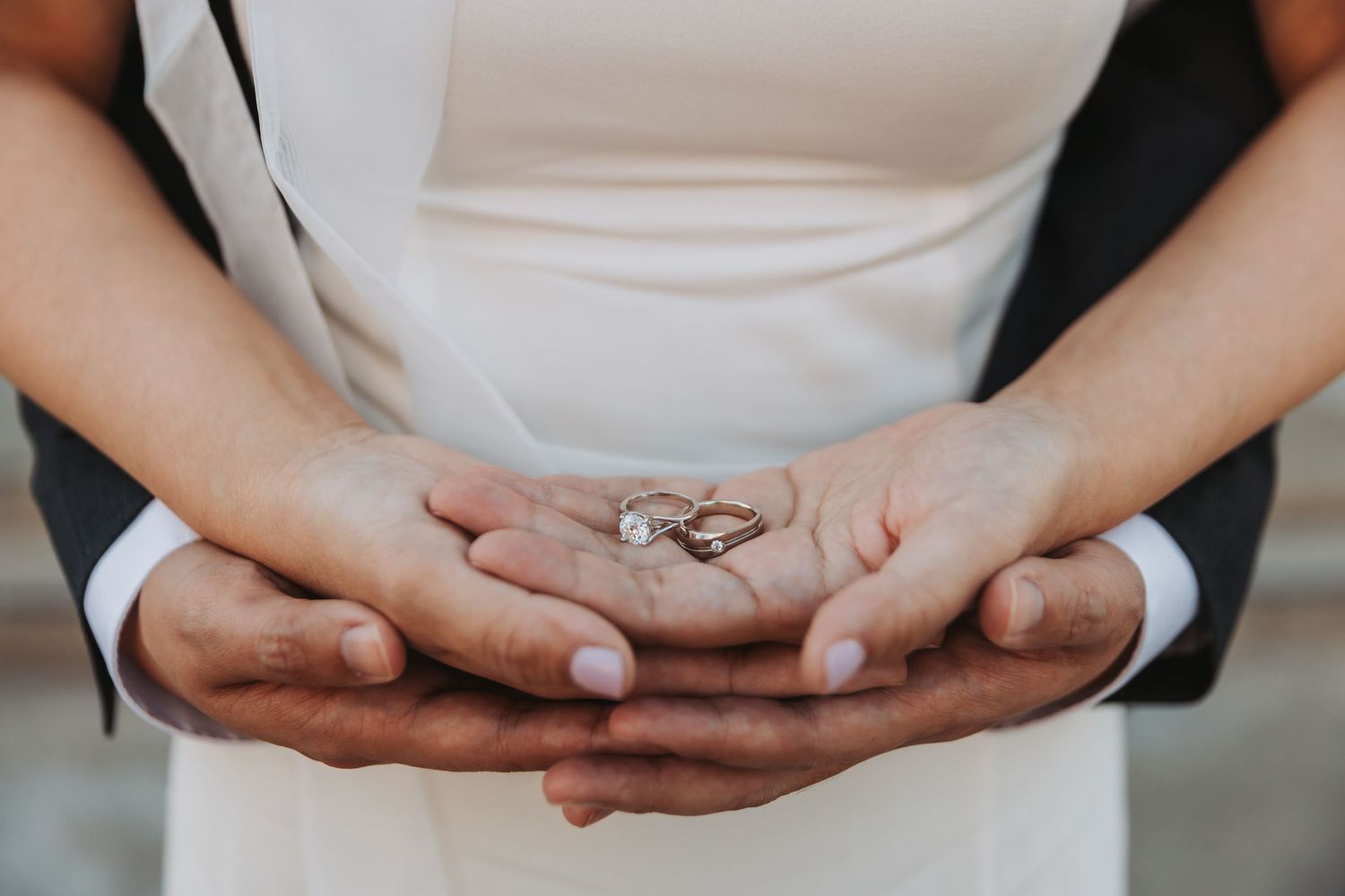 Close-up shot of hands with an engagement ring against a black clothing background.