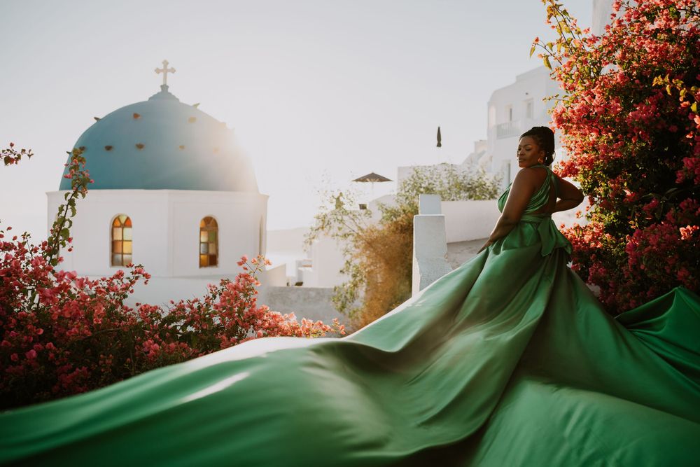 Flowing green dress creates dramatic movement against Santorini church and pink flowers at sunset.