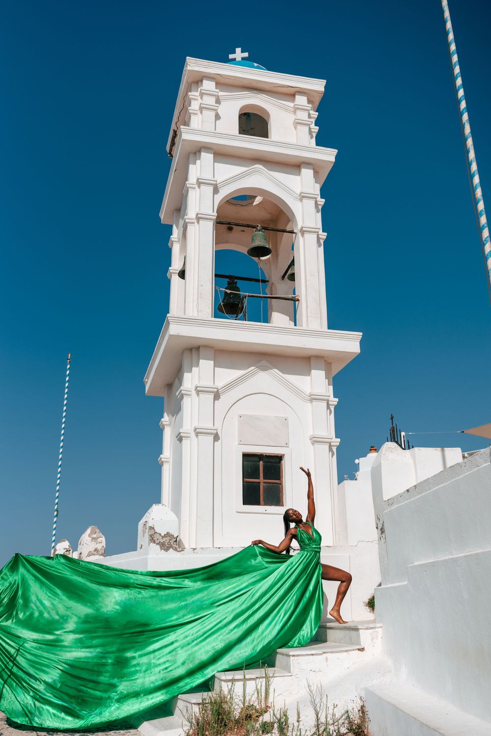 A white bell tower in Santorini with flowing green fabric against bright blue sky.