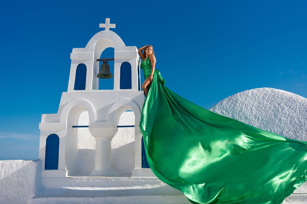 Traditional white Greek bell tower with flowing green fabric billowing in the wind.