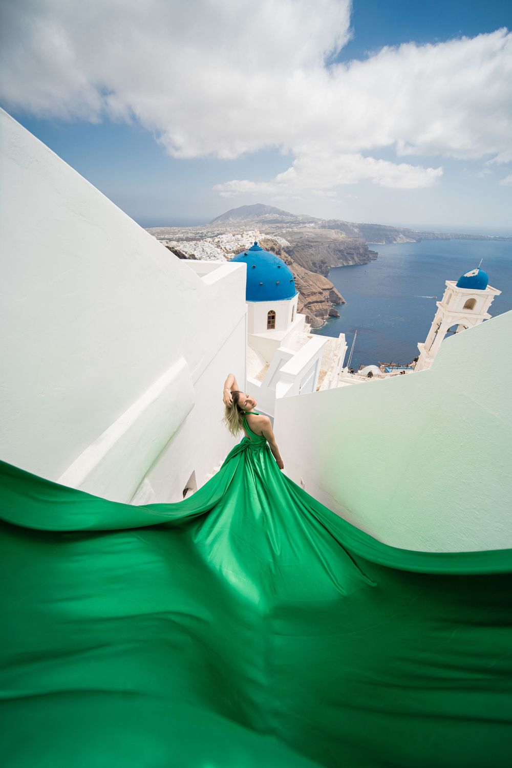Emerald green dress flows dramatically beside blue-domed churches in Santorini.
