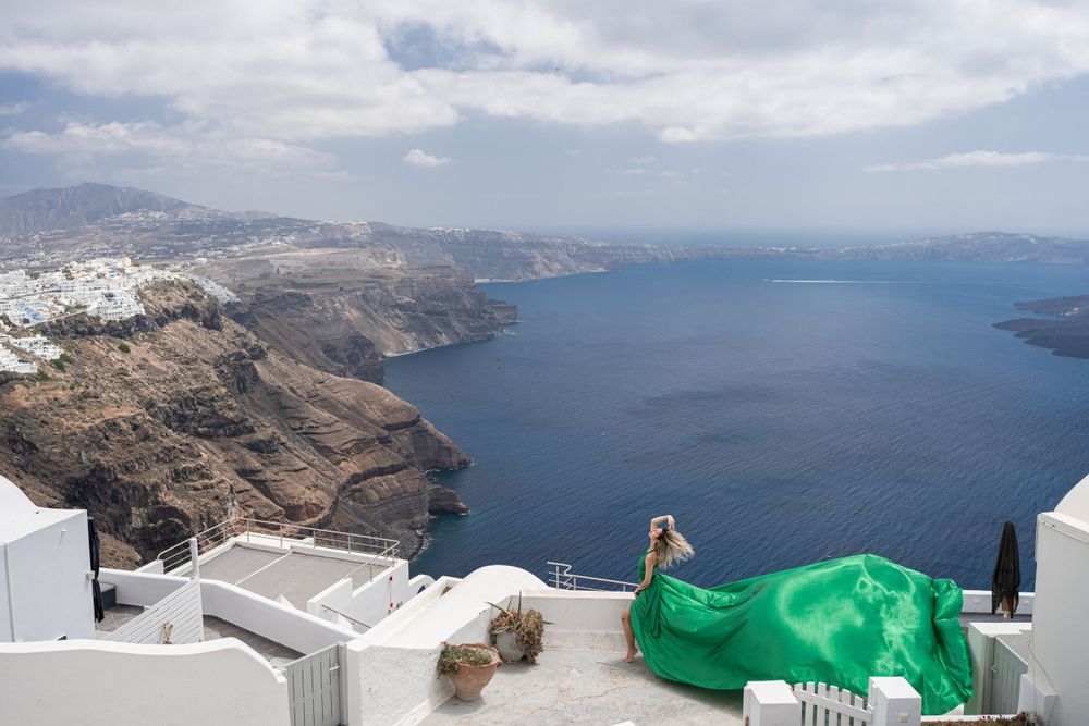 Green fabric flows dramatically on white rooftops overlooking Santorini's volcanic caldera.