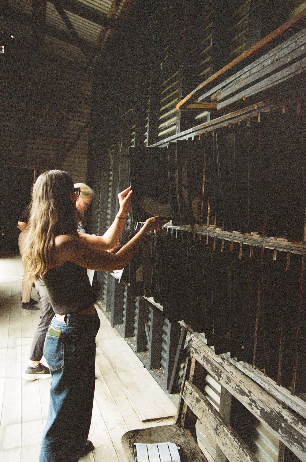 Two people examine old wooden storage shelves in rustic barn interior.