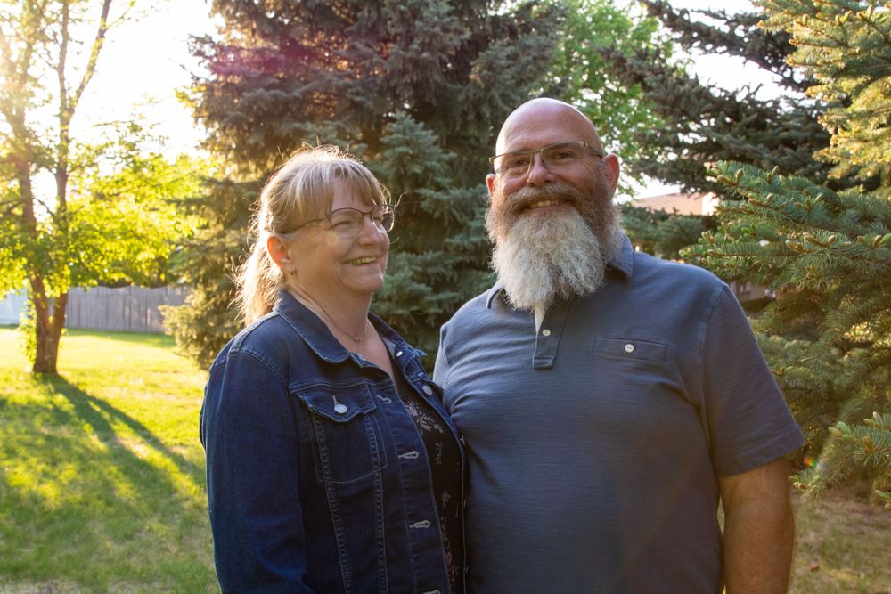 a couple stands together with trees in the background.