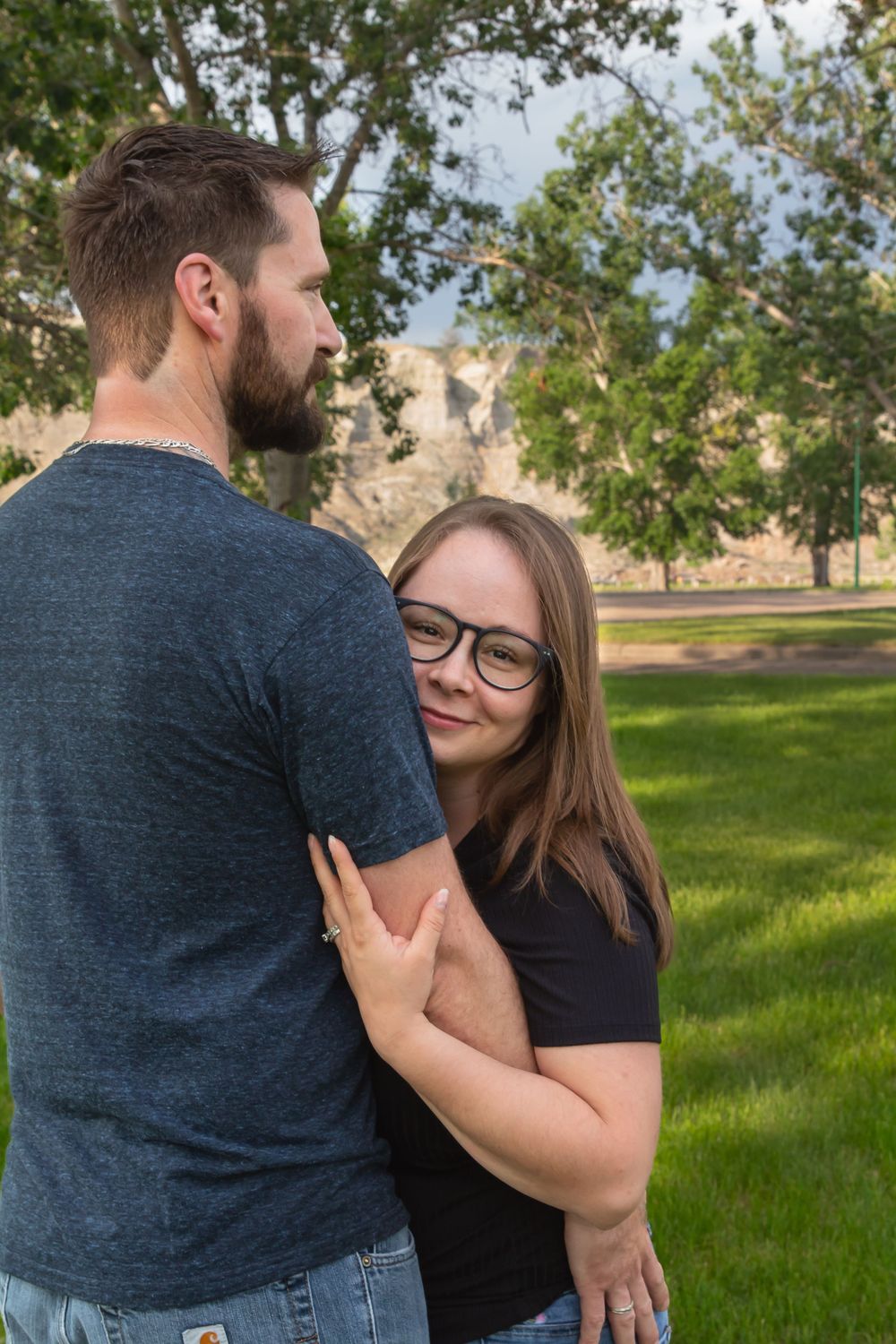 a couple stands together with trees in the background.
