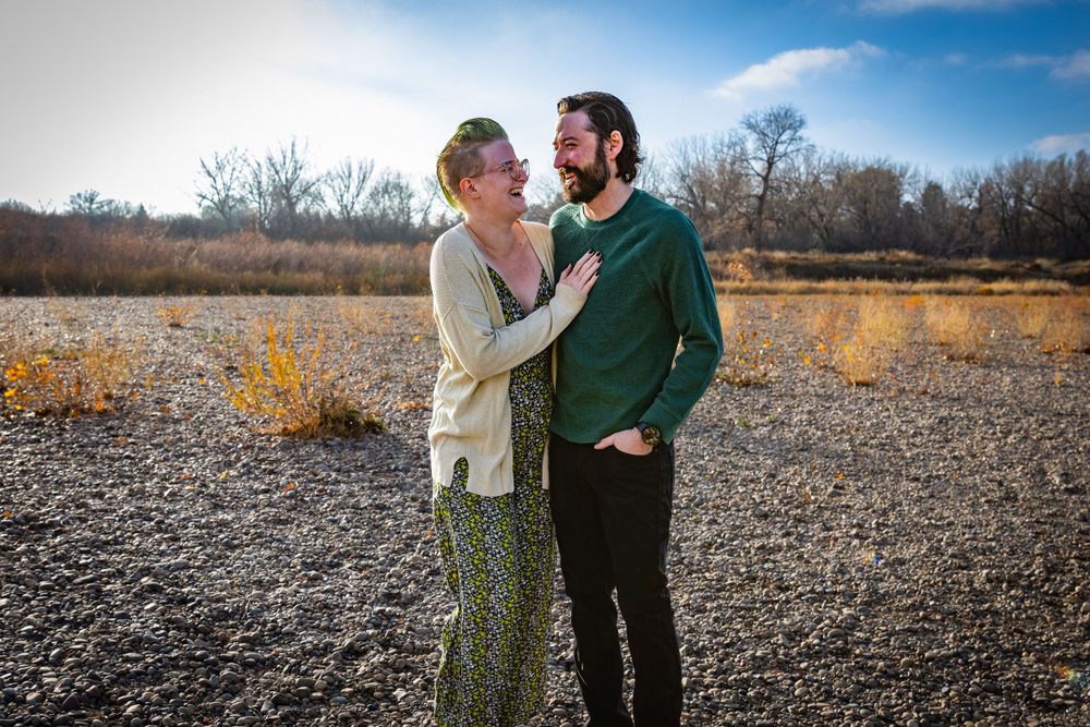 a couple stands together with trees in the background.