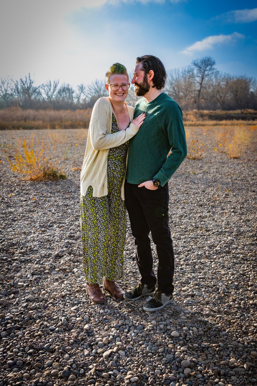 a couple stands together with trees in the background.
