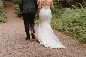 A couple walks down a forest path during their wedding celebration.