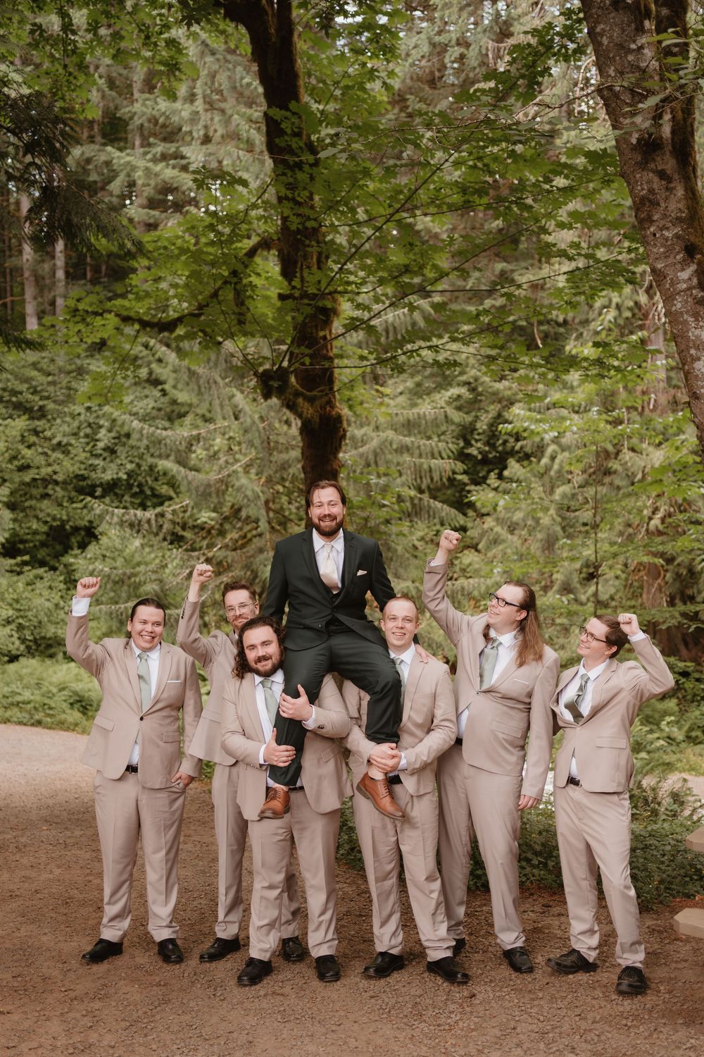 Groomsmen in tan suits strike playful poses for a fun group photo in a forest setting.