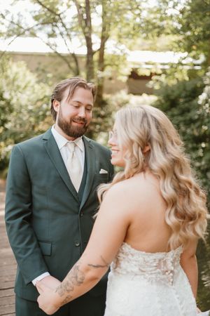 A romantic wedding couple shares an intimate moment in a forest setting wearing a green suit and white dress.