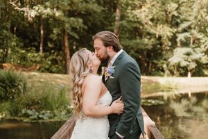 Wedding couple embraces on a wooden deck overlooking a serene pond surrounded by lush greenery.