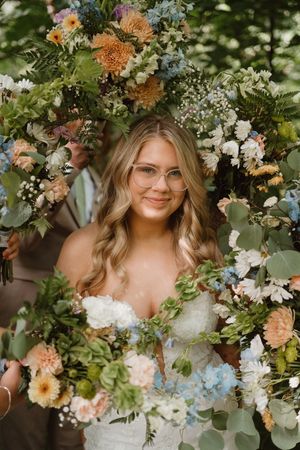 Stunning floral crown with peach, white and blue flowers frames against natural greenery.