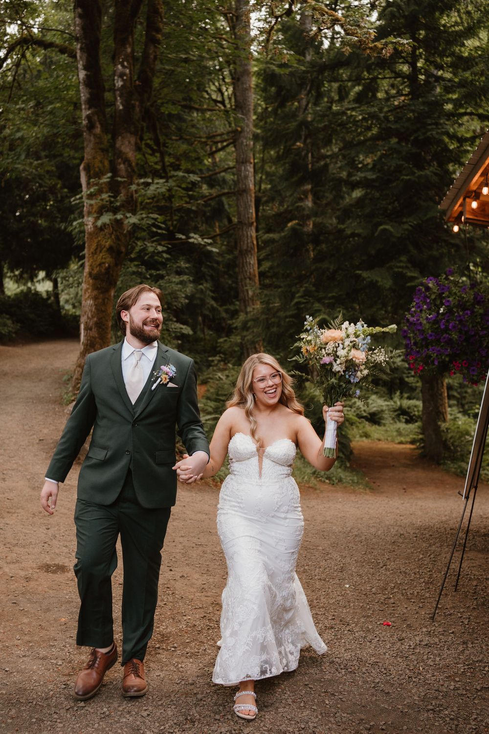Joyful couple walks hand in hand down a forest path at their wedding celebration.
