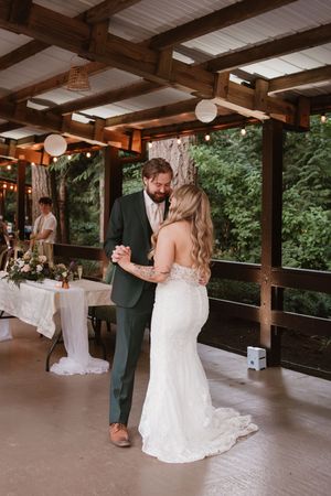A couple shares their first dance under a covered outdoor pavilion at their wedding reception.