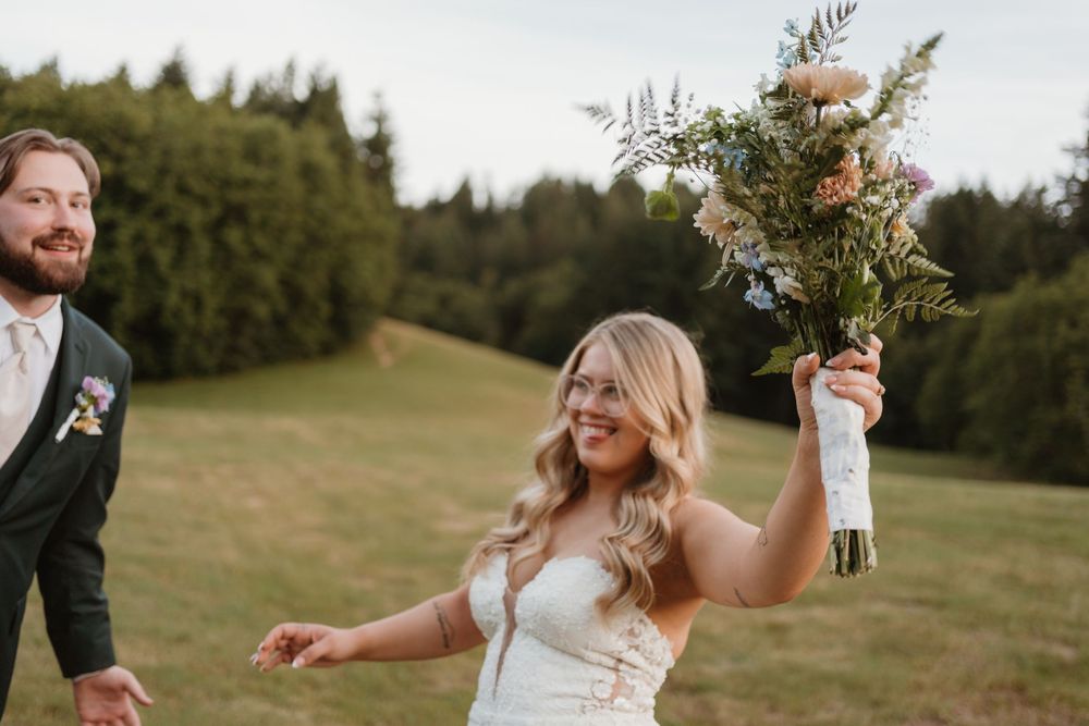 A couple shares candid moments while holding a wildflower bouquet in an outdoor field setting.