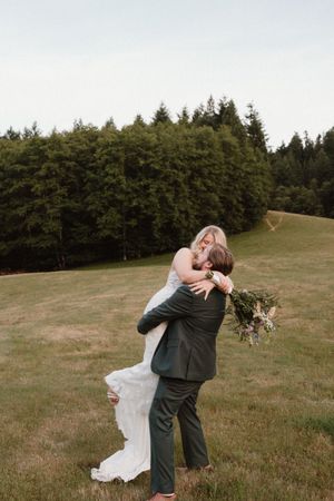 A couple embraces romantically in a sunlit meadow with forest backdrop.
