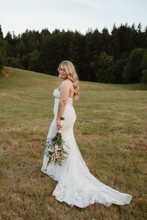 Bride in lace wedding dress twirls in an open field with flowing train.
