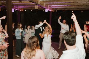 Wedding guests dancing and celebrating under covered outdoor venue with festive lighting.