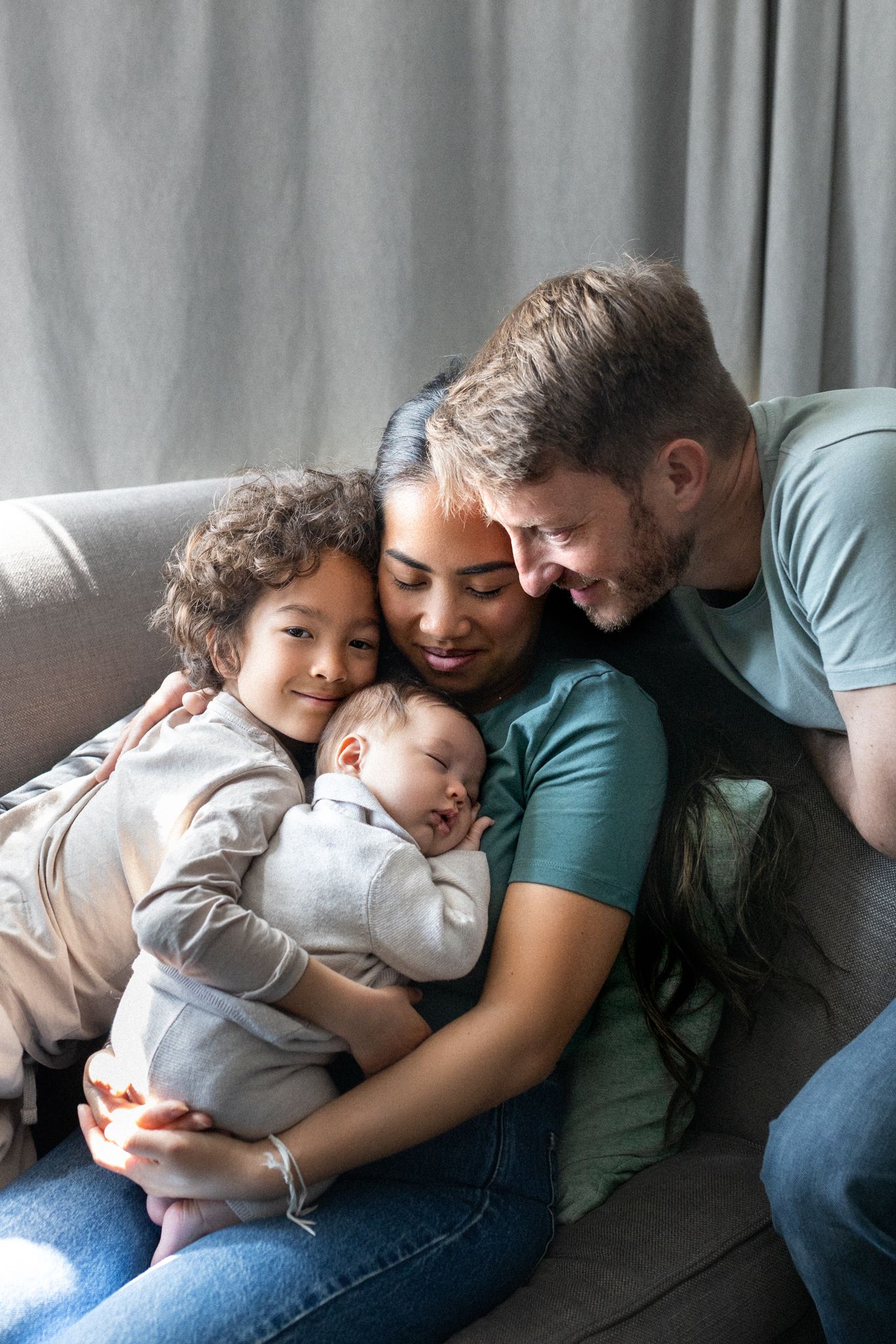 A family sharing a tender cuddle moment together on a gray couch.
