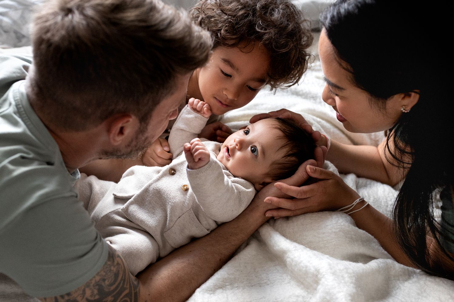 Family gathered together on white bedding sharing an intimate moment with a baby.