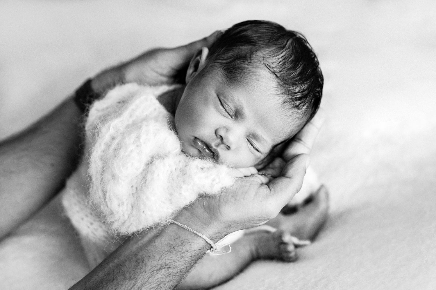 A sleeping newborn baby lies peacefully in soft white blankets against a light background.