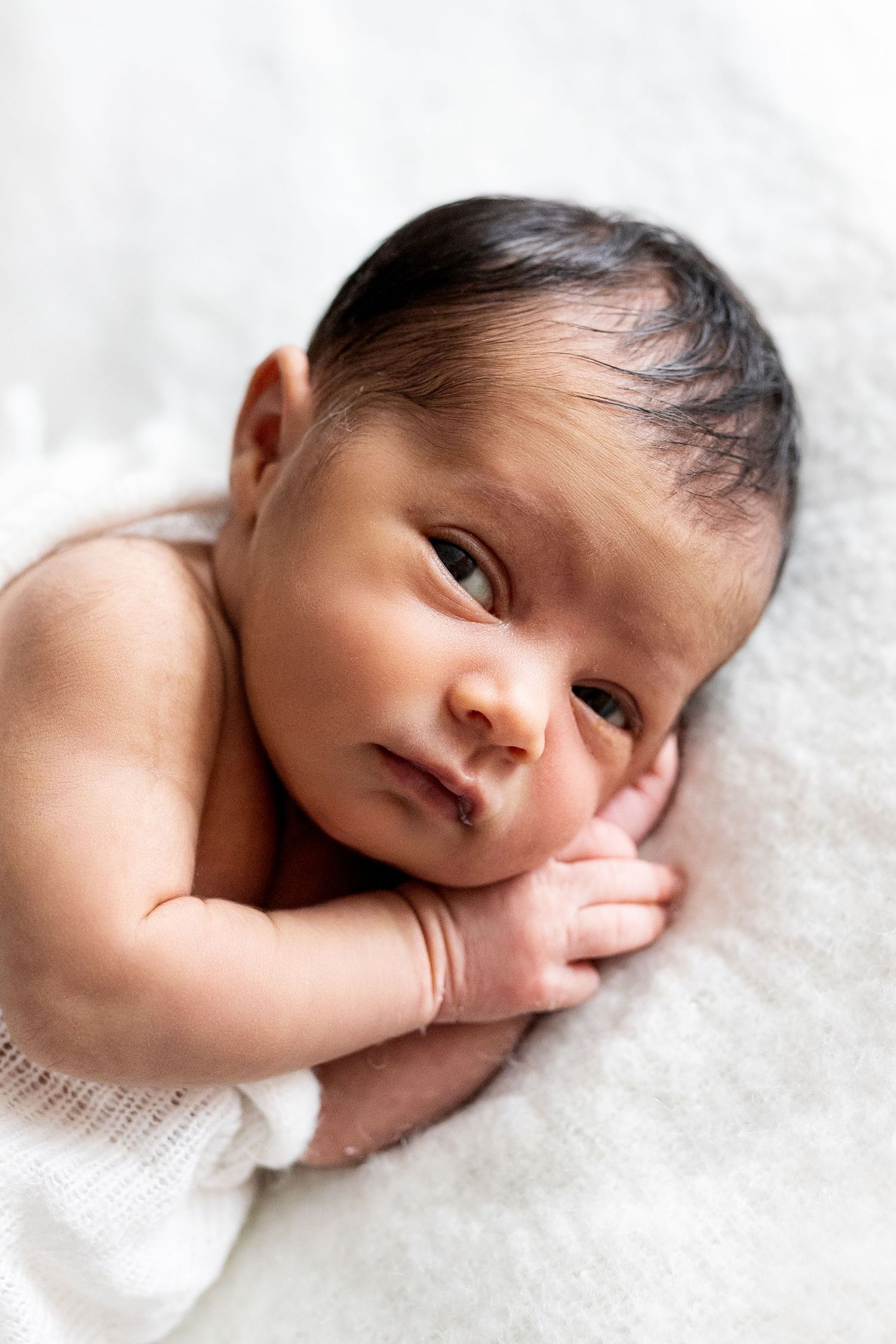 Series of four close-up photos showing a newborn baby resting on soft white fabric.
