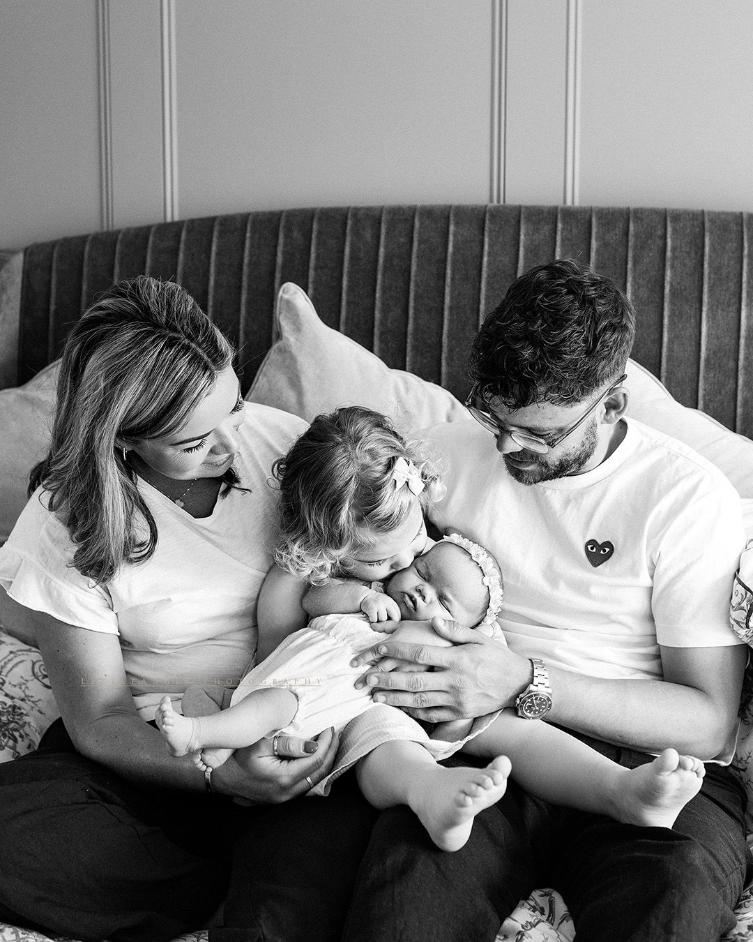 Black and white photo of a family sharing a tender moment with their newborn baby on a gray couch.