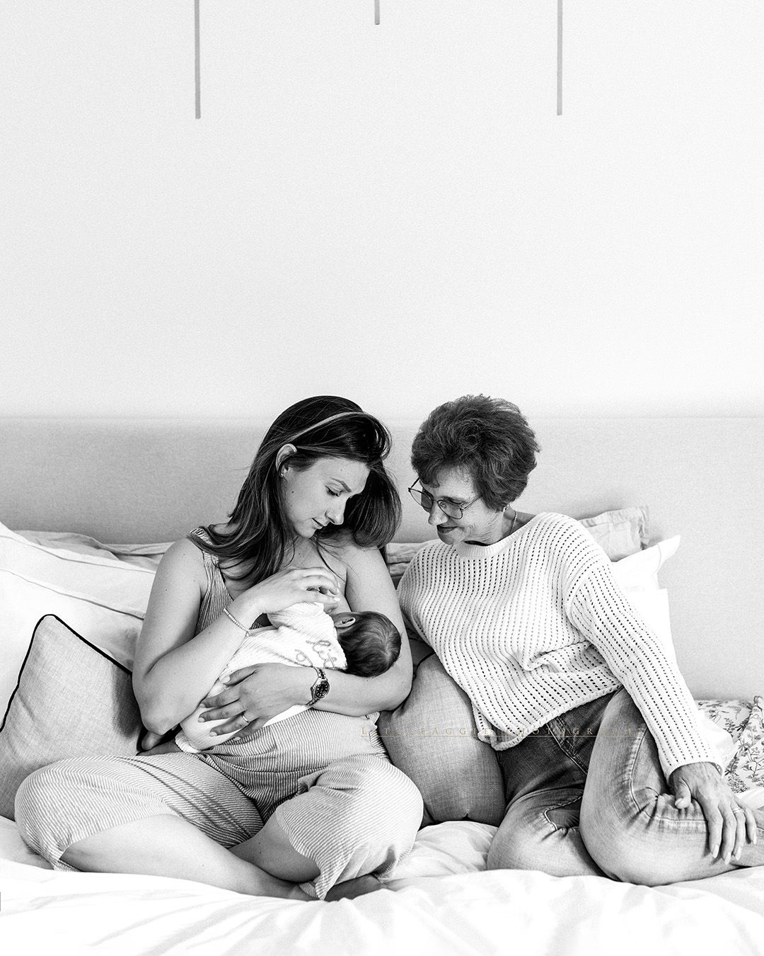 A couple cuddles on a bed together with their newborn baby in a tender black and white moment.